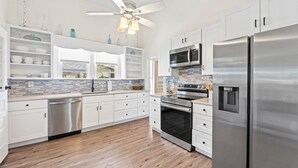 A modern kitchen with white cabinetry, stainless steel appliances, and a wooden floor. - Bay view Historic home walking to St. Joseph Bay and Downtown.  (Port St. Joe)