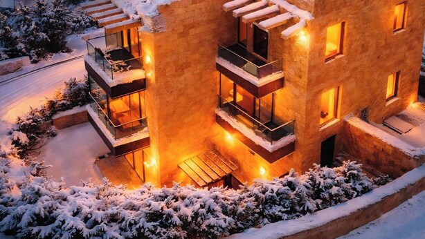 Un edificio moderno de varios pisos con balcones, ventanas iluminadas y alrededores cubiertos de nieve.