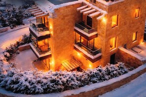 Un edificio moderno de varios pisos con balcones, ventanas iluminadas y alrededores cubiertos de nieve.