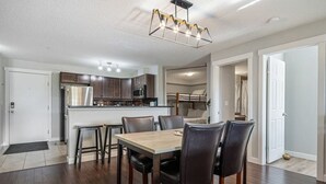 A modern kitchen with dark wood cabinets, a central island, and a dining area with a wooden table and chairs. - Scenic Lakefront Getaway | Hot Tub | Pool | Gym (Invermere)