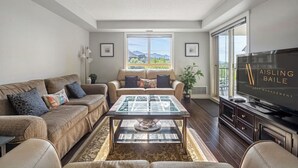 A spacious living room with a large window, a television, and a coffee table. - Scenic Lakefront Getaway | Hot Tub | Pool | Gym (Invermere)