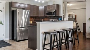 A modern kitchen with stainless steel appliances, a central island with bar stools, and a visible staircase leading to an upper level. - Scenic Lakefront Getaway | Hot Tub | Pool | Gym (Invermere)
