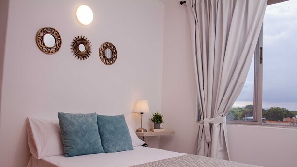 Ein Schlafzimmer mit einem Bett, einem Nachttisch mit Lampe und dekorativen Wandspiegeln.