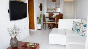Ein modernes Wohnzimmer mit Flachbildfernseher, einem weißen Sofa, einem Couchtisch und einem Essbereich mit Holzstühlen und einem weißen Tisch.