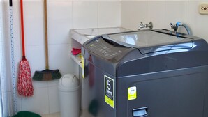 Ein Waschraum mit Waschmaschine, einem Mop, einer Bürste und einem Mülleimer.