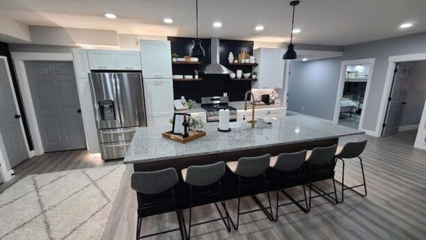 A modern kitchen with a large island, bar stools, stainless steel appliances, and a pendant light.