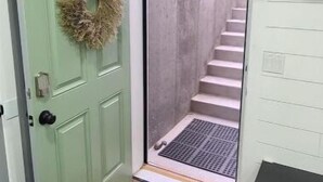 A green door with a wreath, a doormat, a staircase, and a black cabinet.