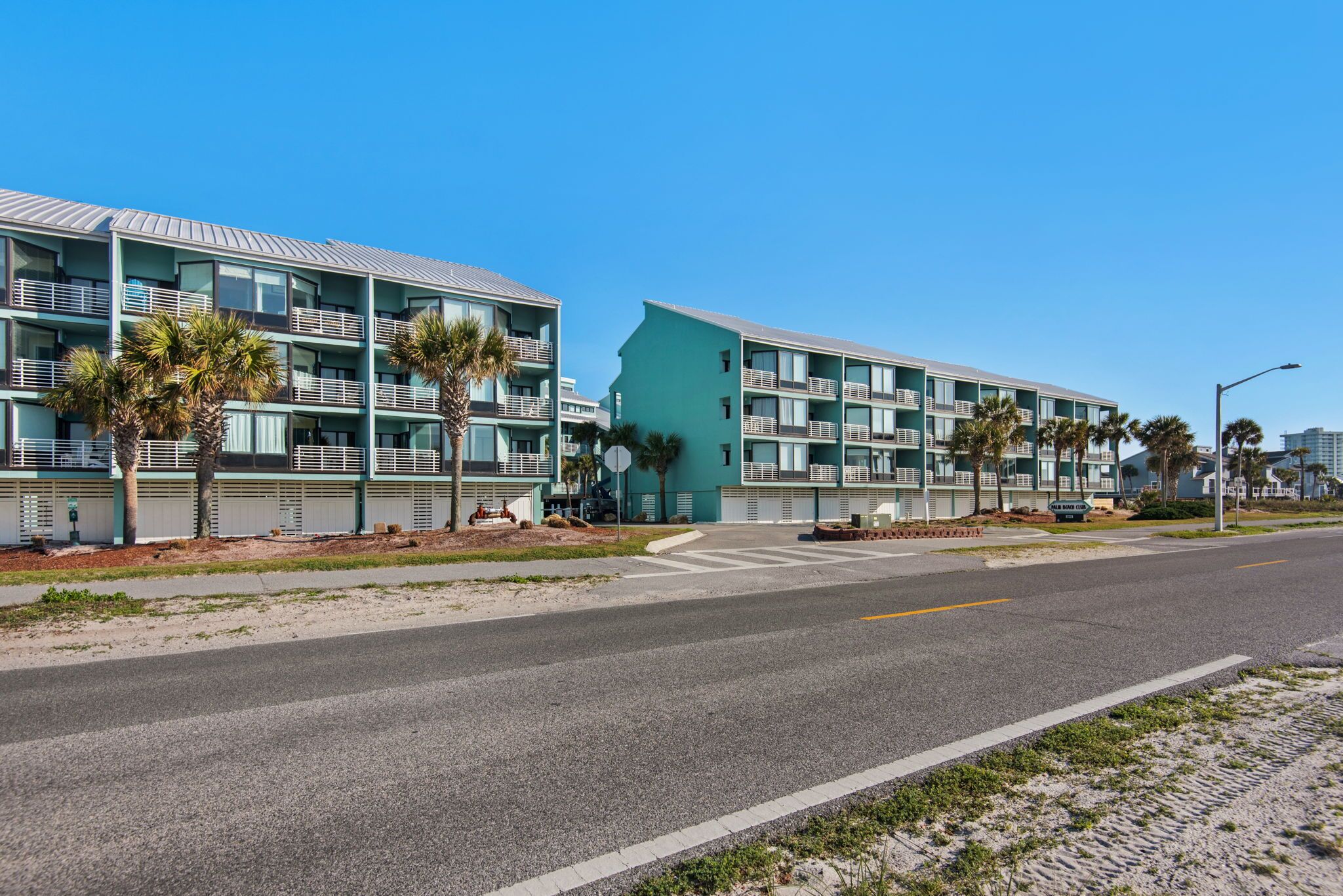 A beachfront hotel with multiple balconies, palm trees, and a clear sky.