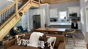 A spacious living area with a wooden staircase, a dining table, and a kitchen with white cabinets and appliances. - Kickback Cabin at Kentucky Lake (Buchanan)