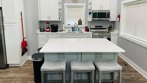A kitchen with white cabinets, a central island with stools, a microwave, and a sink. - Kickback Cabin at Kentucky Lake (Buchanan)