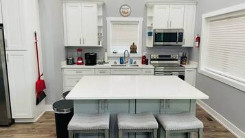 Una cocina con armarios blancos, una isla central con taburetes, un microondas y un fregadero.