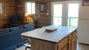 Interior de una cabaña de madera con una isla de cocina, ventilador de techo, refrigerador y un sofá azul.