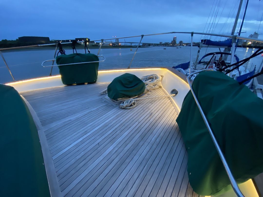 A boat deck with a green cover, ropes, and a view of the water and city skyline.