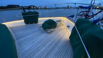 A boat deck with a green cover, ropes, and a view of the water and city skyline.