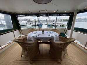 Uma sala de jantar com uma mesa redonda, cadeiras de vime e vista para barcos num porto de recreio.