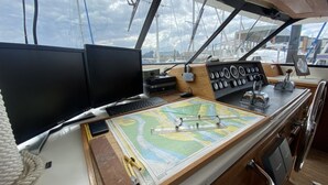 Die Kommandostation eines Bootes mit zwei Monitoren, einem Steuerlenkrad und einer Karte.