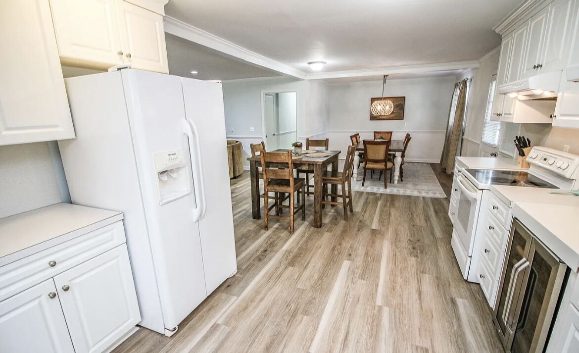 A modern kitchen with white cabinetry, a dining area with wooden chairs, and a central island.