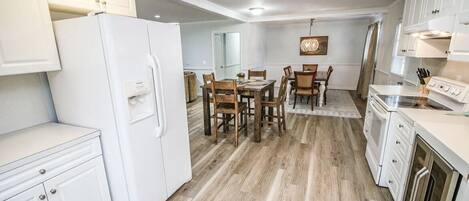 A modern kitchen with white cabinetry, a dining area with wooden chairs, and a central island.