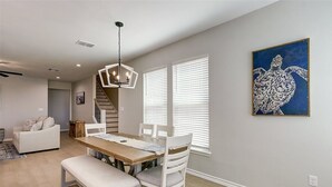 A dining area with a wooden table, white chairs, and a bench. There is a ceiling light fixture above the table.