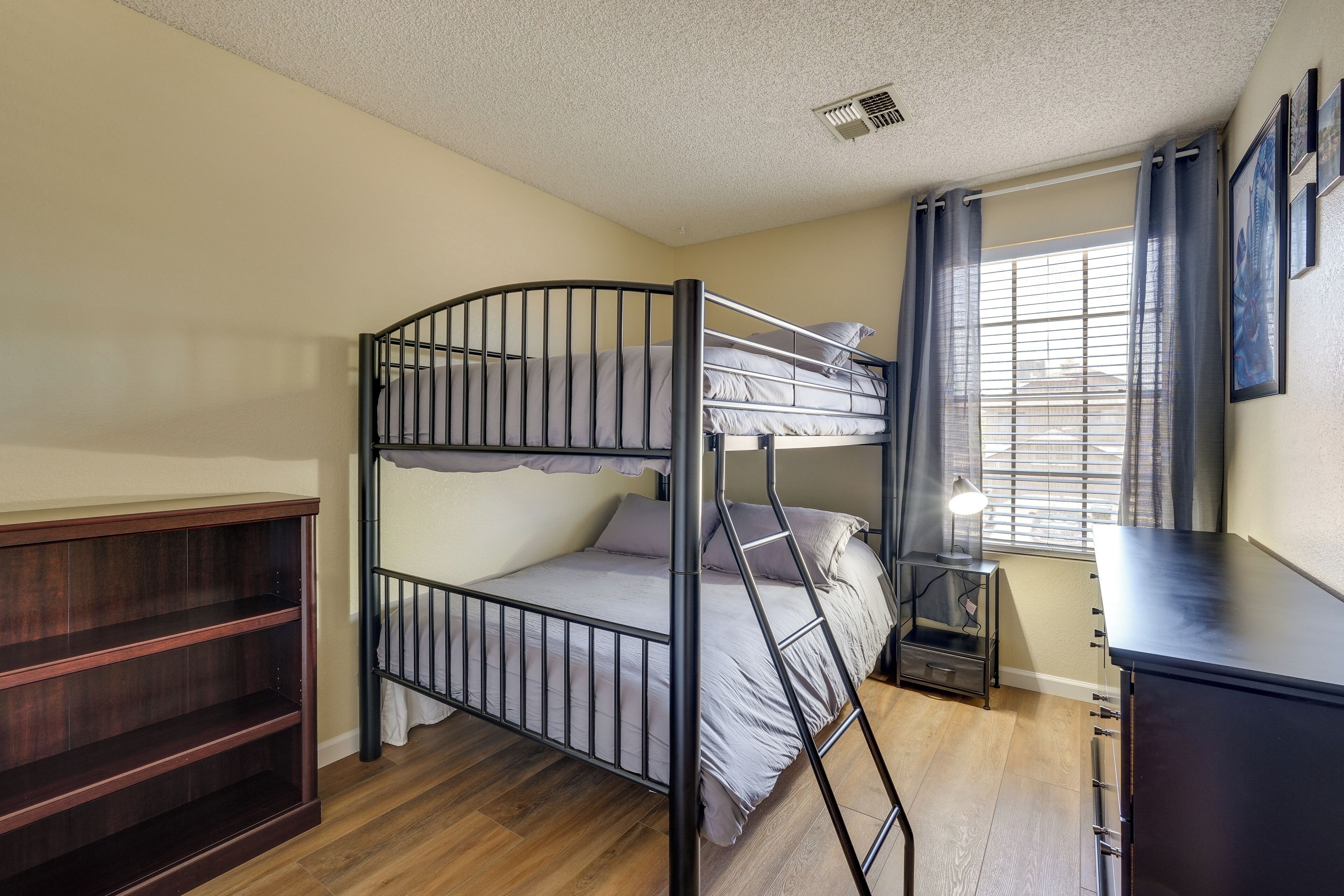 A bunk bed in a room with a wooden floor, a desk, and a window with curtains.