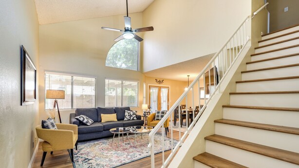 A spacious living room with a dark-colored sofa, a yellow armchair, and a wooden staircase leading to another level. - North Phoenix Home! Great Location + Private Patio (Phoenix)