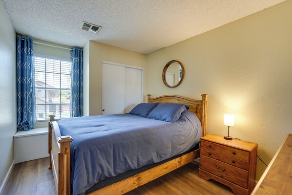 A bedroom with a wooden bed, a bedside table with a lamp, a window with curtains, and a door. - North Phoenix Home! Great Location + Private Patio (Phoenix)