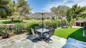 A patio with a table and chairs, an umbrella, and a view of a golf course. - Phoenix Home on Golf Course: Pool & Hot Tub Access (Phoenix)