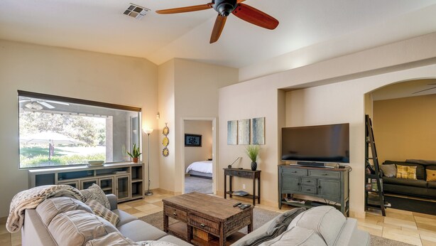 A spacious living room with a large window, a ceiling fan, a television, and a sofa. - Phoenix Home on Golf Course: Pool & Hot Tub Access (Phoenix)