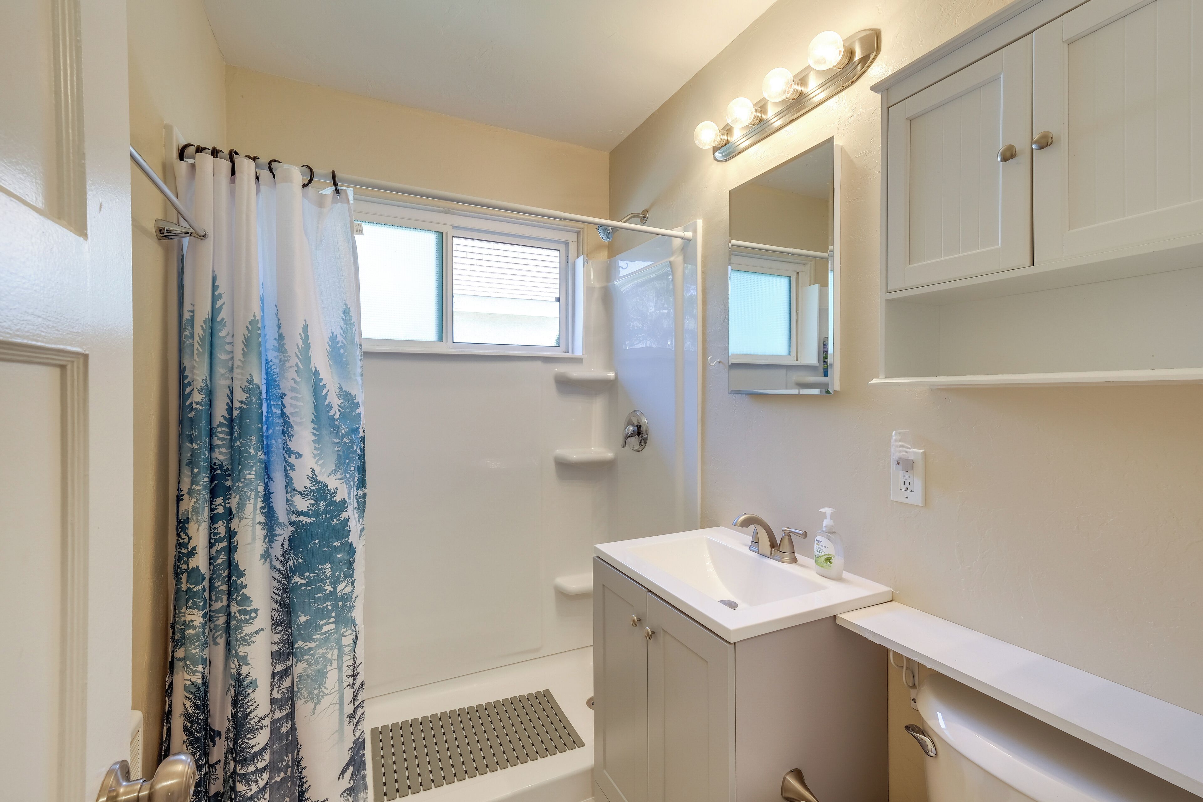 A bathroom with a shower, a sink, a mirror, and a window.