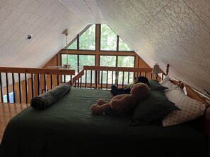 An attic bedroom with a sloped ceiling, large windows, a wooden bed frame, and a green bedspread.