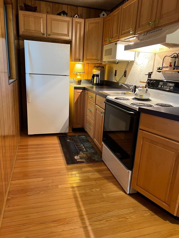 A kitchen with wooden cabinets, a white refrigerator, a stove, a microwave, and a coffee maker.