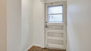 Een witte deur met een raam, een zichtbare pijp erboven en een houten vloer.
