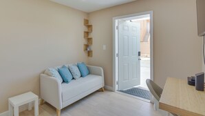 A modern living room with a white sofa, a small white table, a wooden shelf unit, and a door leading outside. - Refreshing Miami Apartment: 4 Mi to the Beach! (Miami)