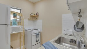 A compact kitchen with a microwave, stove, sink, and a window with blinds. - Refreshing Miami Apartment: 4 Mi to the Beach! (Miami)