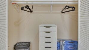 A closet with a white storage unit, a hanging rod with black hangers, and a trash bin. - Refreshing Miami Apartment: 4 Mi to the Beach! (Miami)