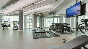 A modern gym with various exercise equipment, large windows, and a flat-screen TV.