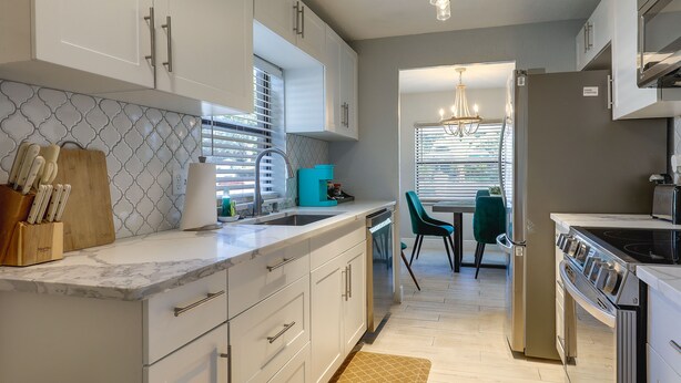 A modern kitchen with white cabinetry, a marble countertop, a built-in oven, and a dining area with a table and chairs. - Tampa Home w/ Patio - 1 Mi to Busch Gardens! (Tampa)