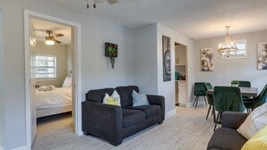 A modern living room with a dark sofa, a dining area with green chairs, and a kitchen in the background. - Tampa Home w/ Patio - 1 Mi to Busch Gardens! (Tampa)