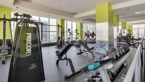 Uma academia com diversos equipamentos de exercício, amplas janelas e vista para a cidade.