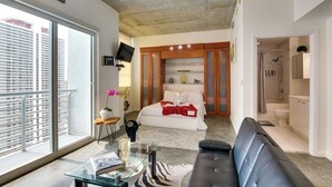 Quarto moderno com uma janela grande, mesa de centro de vidro, sofá de couro preto e guarda-roupa de madeira.