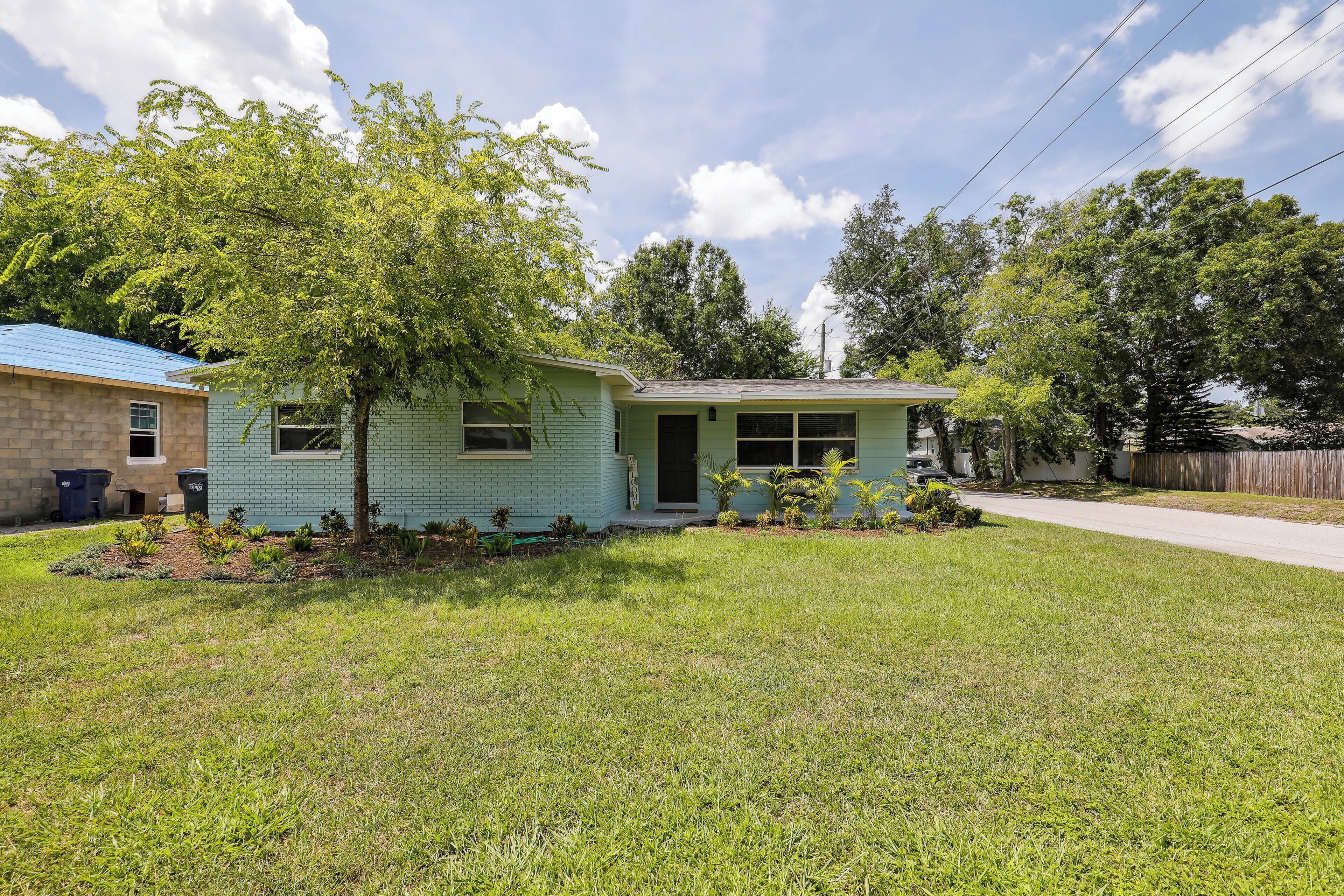 A single-story house with a front yard, a small tree, and a neighboring building.