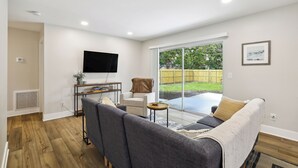 Una sala de estar moderna con un sofá gris, un sillón blanco y un televisor de pantalla plana montado en la pared.