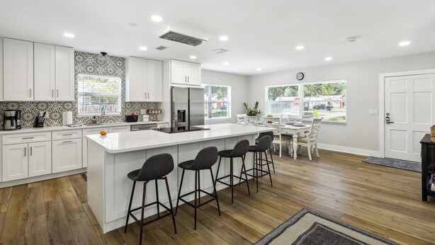 Una cocina moderna con armarios blancos, una isla central con taburetes, un refrigerador y un comedor con mesa y sillas.