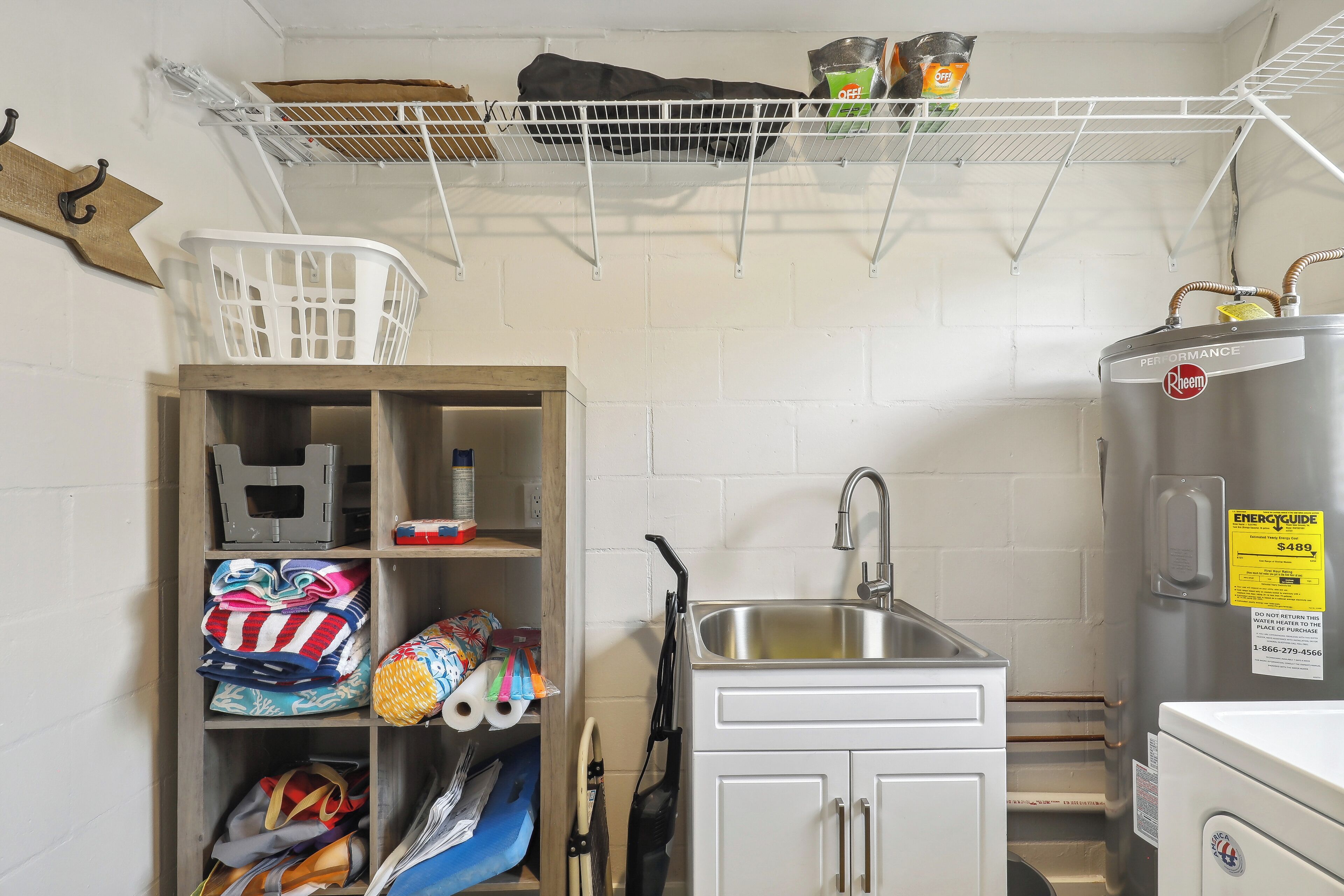 A compact kitchen with a sink, a refrigerator, and a storage unit with folded clothes and bags.