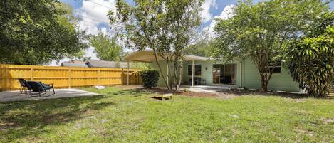 A backyard with a lawn, a wooden fence, a small tree, and a building with a door and windows.
