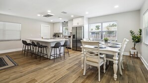 Una cocina moderna con una isla central, taburetes de bar, una mesa de comedor y una nevera.