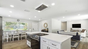 Una cocina moderna con armarios blancos, horno empotrado y comedor con sillas y mesa blancos.
