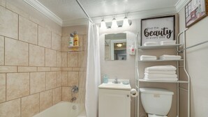A bathroom with a bathtub, toilet, and shelves with towels. - Downtown Jacksonville Studio w/ City Views! (Jacksonville)