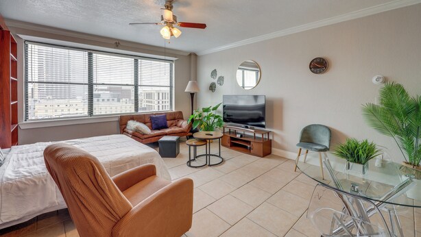 A modern living room with a bed, sofa, TV, and glass dining table. - Downtown Jacksonville Studio w/ City Views! (Jacksonville)