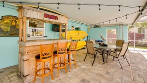 A wooden bar with a surfboard, chairs, and a table with a bird on it. - Canal-front Tampa Vacation Rental w/ Private Pool! (Tampa)